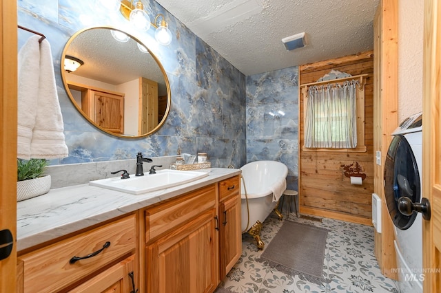 full bathroom with a textured ceiling, a soaking tub, vanity, and washer / dryer