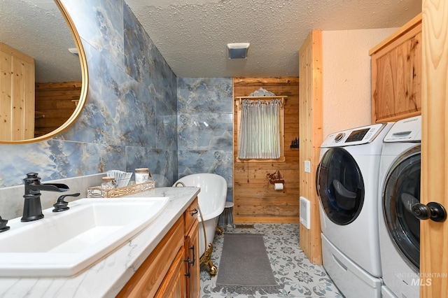 full bathroom with a tub, a textured ceiling, vanity, wood walls, and washing machine and dryer