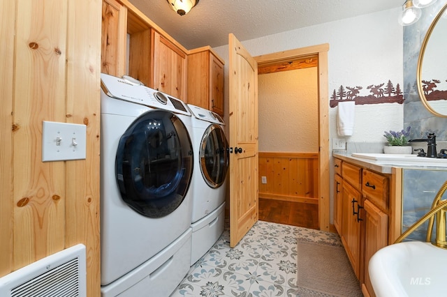 clothes washing area with wooden walls, a wainscoted wall, washing machine and clothes dryer, a textured ceiling, and a sink