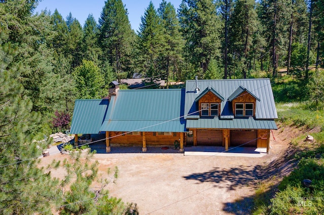 view of front of house featuring metal roof, an attached garage, driveway, a chimney, and a wooded view