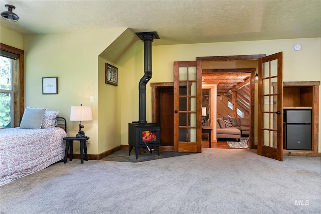 carpeted bedroom featuring a wood stove, a textured ceiling, french doors, and fridge