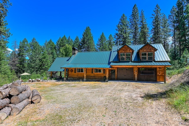 view of front of property featuring driveway, a standing seam roof, a chimney, and metal roof