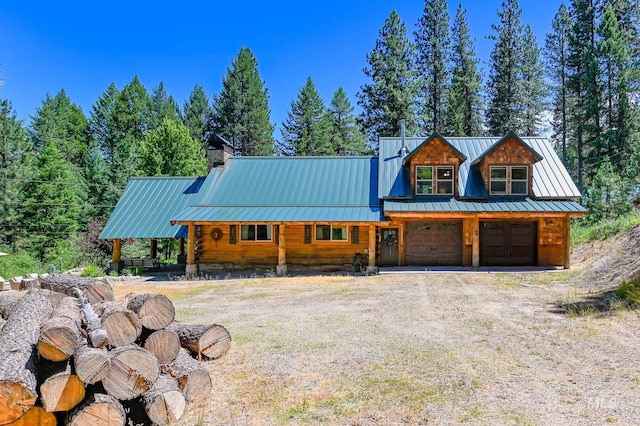 view of front of house with dirt driveway, a chimney, metal roof, an attached garage, and a standing seam roof