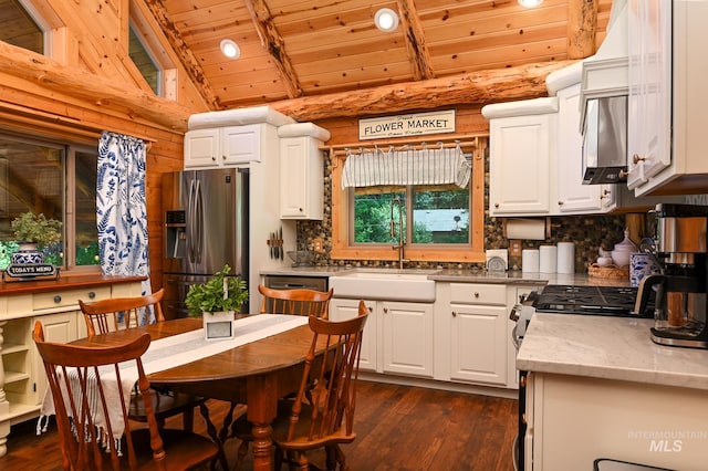 kitchen with vaulted ceiling with beams, dark wood-type flooring, wood ceiling, white cabinets, and stainless steel fridge