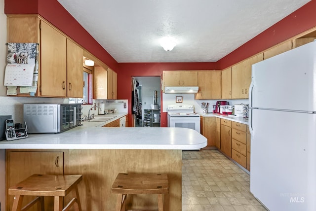 kitchen with sink, a kitchen bar, white appliances, kitchen peninsula, and a textured ceiling