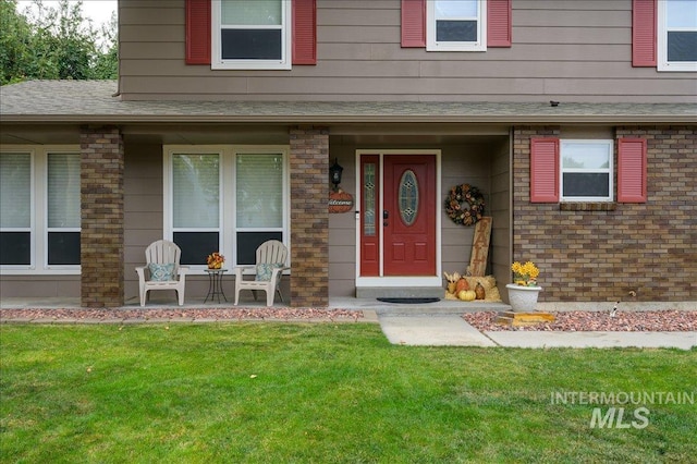 view of exterior entry featuring covered porch, roof with shingles, and a yard