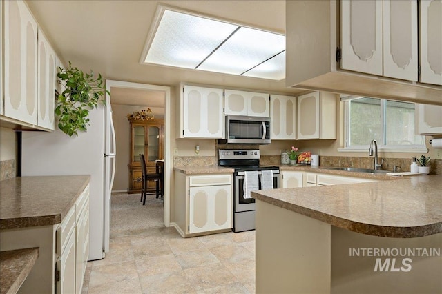 kitchen with a peninsula, white cabinetry, appliances with stainless steel finishes, and a sink