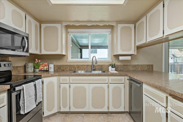 kitchen with white cabinetry, stainless steel appliances, a sink, and light countertops