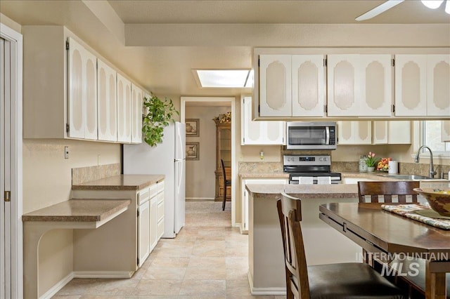 kitchen with a skylight, white cabinets, appliances with stainless steel finishes, light countertops, and a sink