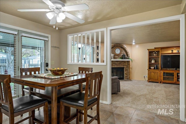 carpeted dining area with a textured ceiling, ceiling fan, and a fireplace