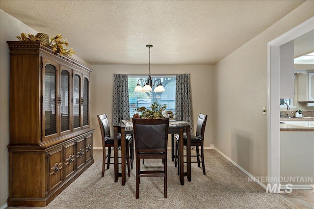 dining room with a textured ceiling, baseboards, a notable chandelier, and light colored carpet