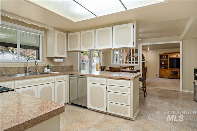 kitchen featuring dishwasher, a peninsula, light countertops, white cabinetry, and a sink