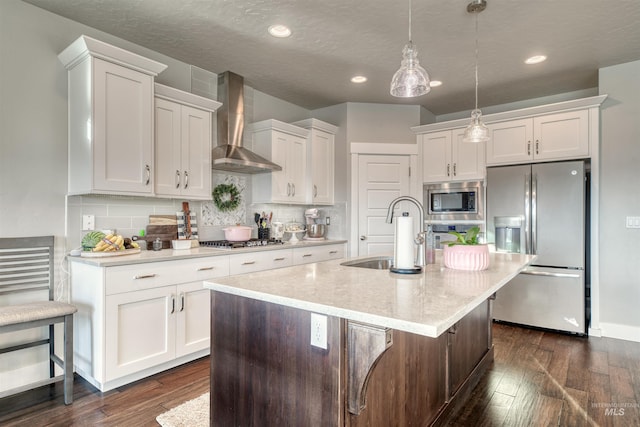 kitchen with dark wood-style flooring, a sink, wall chimney range hood, white cabinets, and appliances with stainless steel finishes