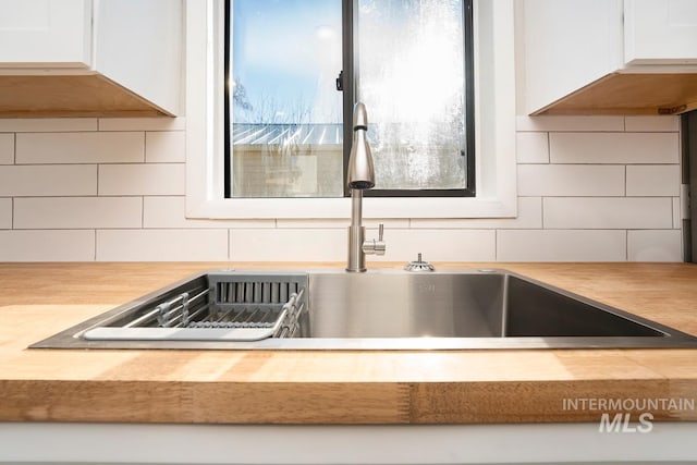 interior details with sink, backsplash, and white cabinetry