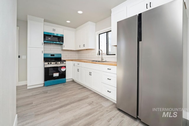 kitchen with sink, white cabinetry, light wood-type flooring, butcher block countertops, and appliances with stainless steel finishes