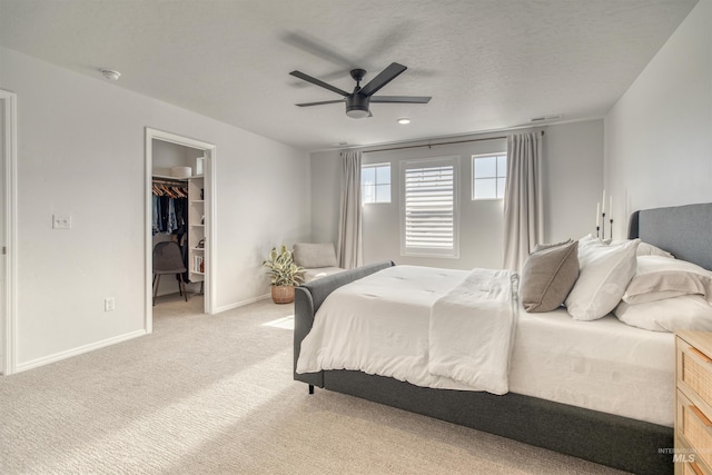 bedroom with a walk in closet, light colored carpet, baseboards, ceiling fan, and a closet