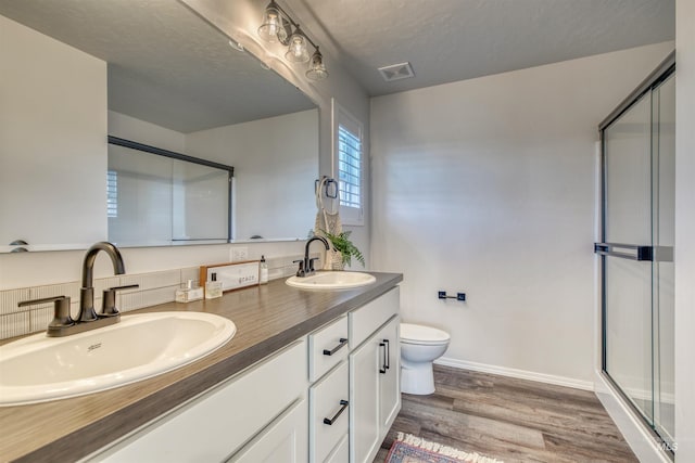 bathroom with a shower stall, toilet, wood finished floors, double vanity, and baseboards