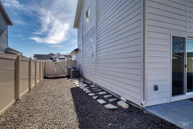 view of property exterior with a gate, central air condition unit, and fence