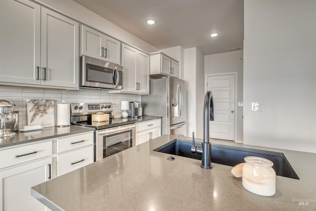 kitchen with appliances with stainless steel finishes, backsplash, recessed lighting, a sink, and dark countertops