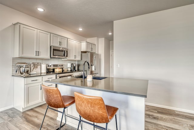 kitchen featuring appliances with stainless steel finishes, light wood-style flooring, a sink, dark countertops, and recessed lighting