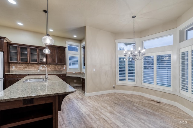 13569 Paoletti St, Caldwell, ID 83607 - kitchen featuring light wood-style floors, dark brown cabinets, decorative backsplash, a chandelier, and glass insert cabinets