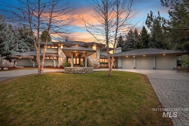 prairie-style home featuring a yard, a chimney, stone siding, driveway, and an outdoor structure