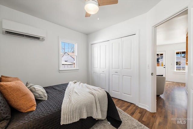 bedroom featuring a ceiling fan, wood finished floors, baseboards, a closet, and a wall mounted air conditioner