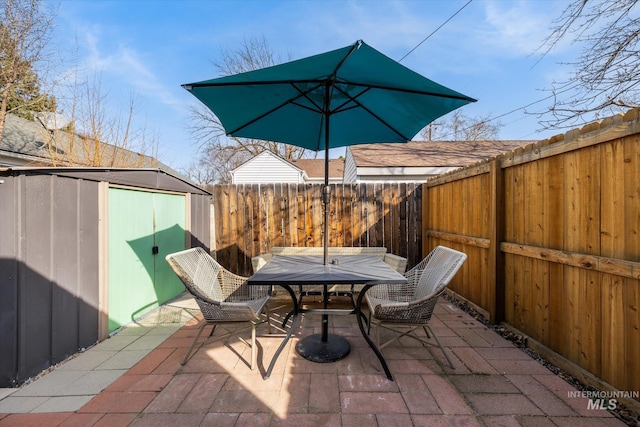 view of patio / terrace featuring a fenced backyard, an outbuilding, outdoor dining space, and a shed