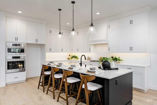 kitchen with a center island with sink, white cabinets, stainless steel double oven, and light hardwood / wood-style floors