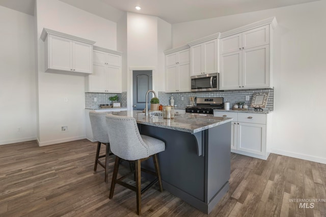 kitchen with a kitchen island with sink, white cabinets, decorative backsplash, appliances with stainless steel finishes, and wood-type flooring