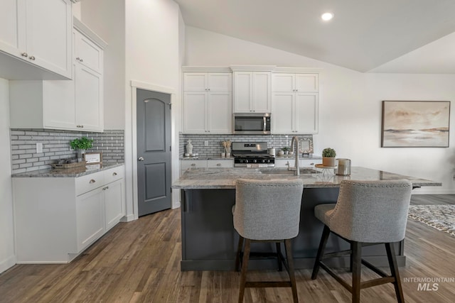 kitchen featuring vaulted ceiling, white cabinetry, stainless steel appliances, and light stone counters