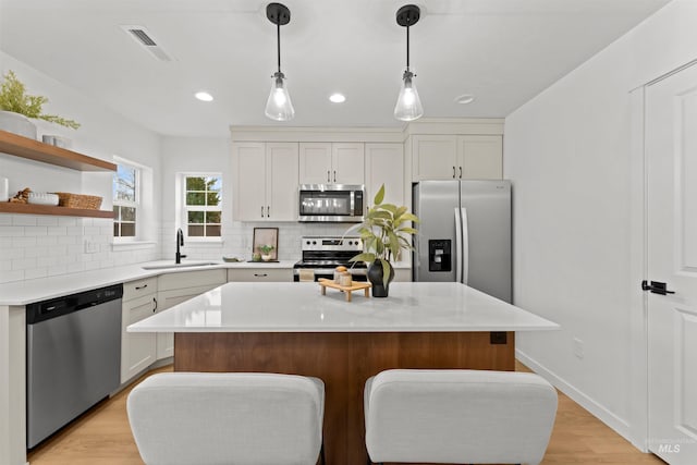 kitchen with a center island, sink, hanging light fixtures, white cabinetry, and stainless steel appliances