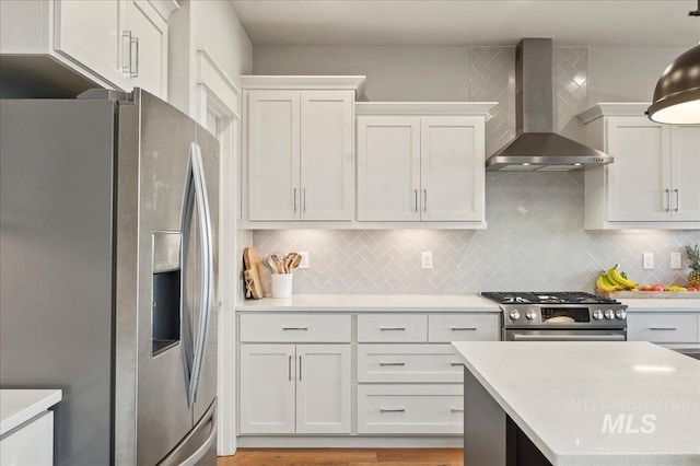 kitchen featuring stainless steel appliances, light countertops, wall chimney range hood, white cabinetry, and backsplash