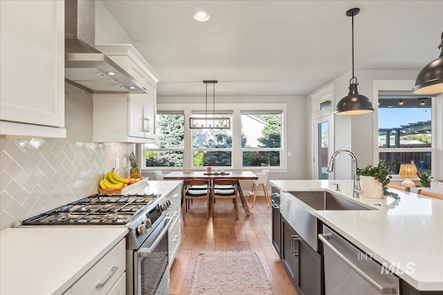 kitchen with wall chimney range hood, appliances with stainless steel finishes, light countertops, and backsplash