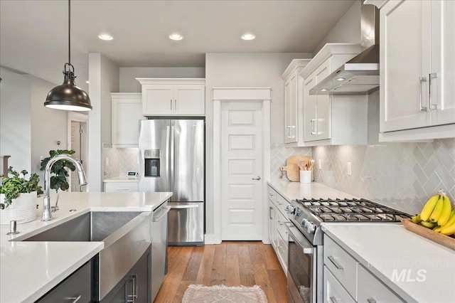 kitchen featuring wall chimney range hood, a sink, appliances with stainless steel finishes, and white cabinets