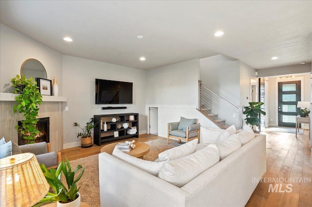 living room with stairs, a tiled fireplace, light wood-style flooring, and recessed lighting