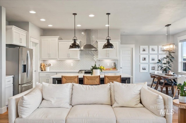 kitchen with white cabinets, stainless steel fridge with ice dispenser, open floor plan, light countertops, and wall chimney range hood