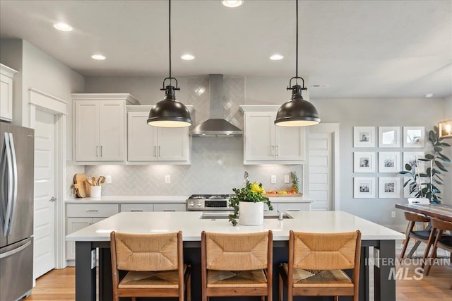 kitchen featuring tasteful backsplash, a kitchen island with sink, stainless steel appliances, light countertops, and wall chimney range hood