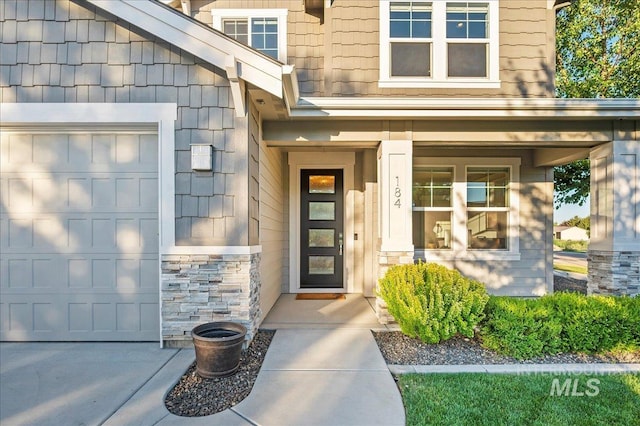 view of exterior entry featuring a garage, stone siding, and covered porch