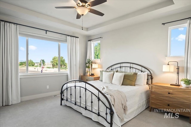 bedroom featuring a tray ceiling, carpet, a ceiling fan, and baseboards