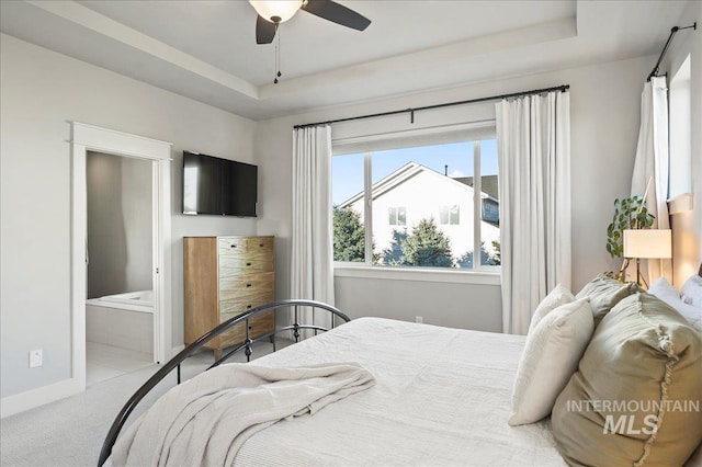 carpeted bedroom with a ceiling fan, a tray ceiling, ensuite bath, and baseboards