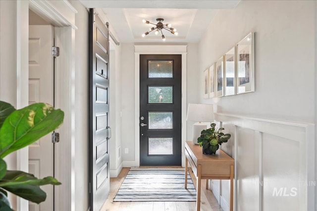 entrance foyer featuring light wood finished floors, a tray ceiling, and a barn door