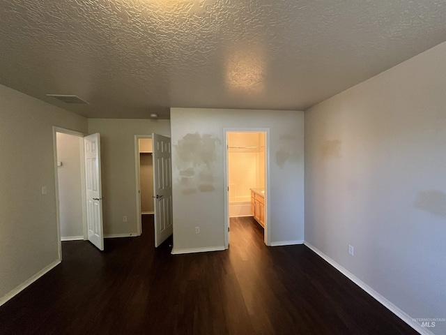 unfurnished bedroom with dark wood-style flooring, a walk in closet, a textured ceiling, baseboards, and a closet