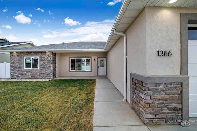 property entrance with stucco siding, a shingled roof, a lawn, fence, and stone siding