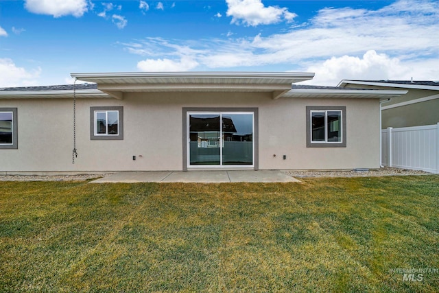 rear view of house featuring stucco siding, fence, a lawn, and a patio