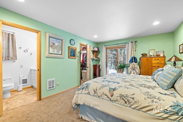 bedroom with a spacious closet, light colored carpet, ensuite bathroom, and a closet