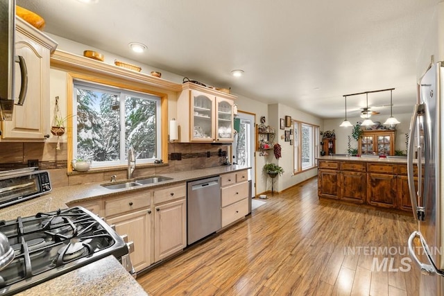 kitchen with light hardwood / wood-style floors, stainless steel appliances, tasteful backsplash, decorative light fixtures, and sink