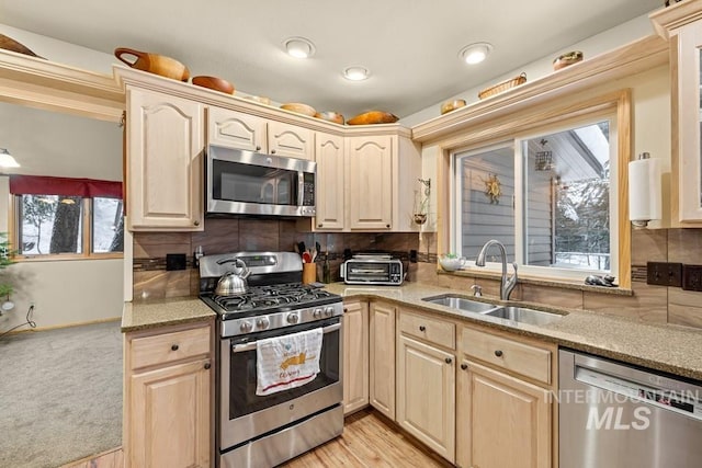 kitchen featuring stainless steel appliances, backsplash, light brown cabinetry, light hardwood / wood-style flooring, and sink