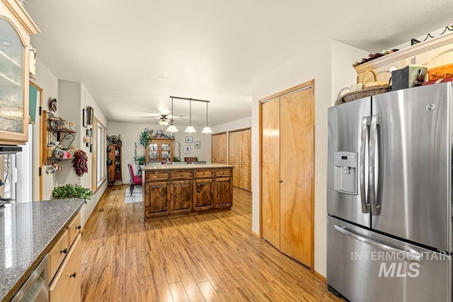 kitchen with stainless steel appliances, dark stone counters, hanging light fixtures, light wood-type flooring, and ceiling fan