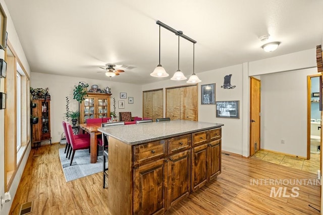 kitchen with ceiling fan, decorative light fixtures, light hardwood / wood-style flooring, light stone counters, and a center island